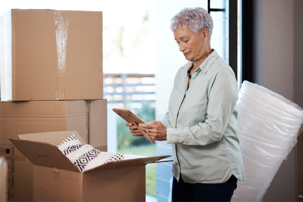 Une femme âgée regardant un cadre photo alors qu'elle emballe des objets dans des cartons de déménagement.