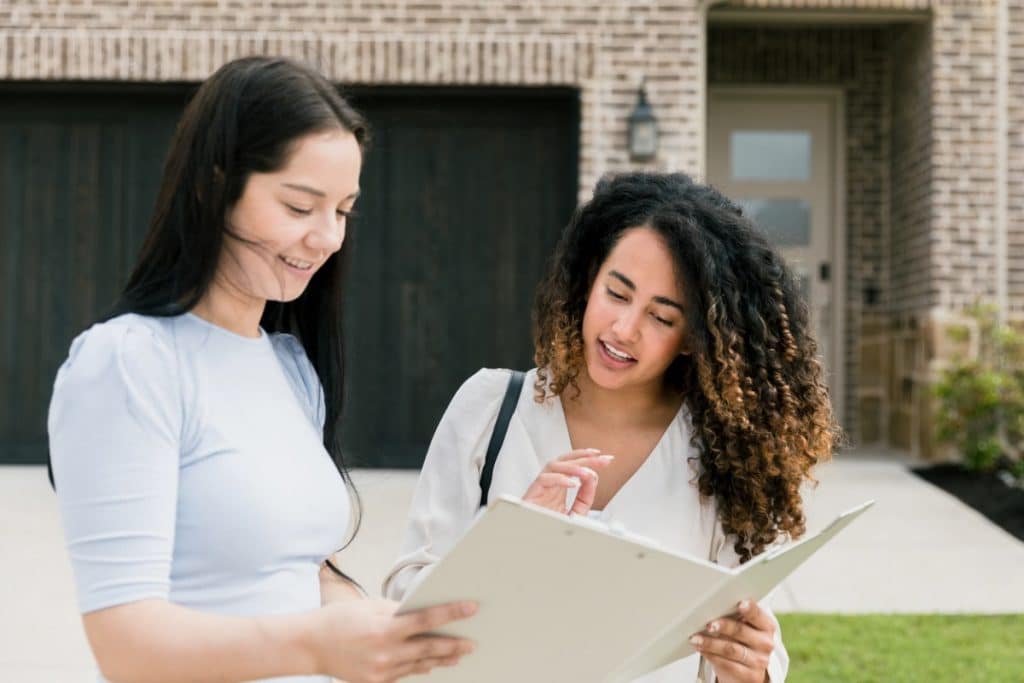 Deux jeunes femmes discutant de la paperasse devant une maison.