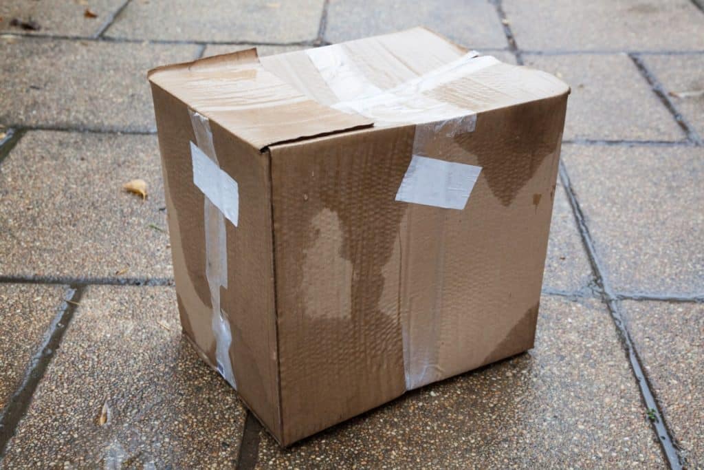 Une boîte en carton humide et endommagée posée sur le trottoir.